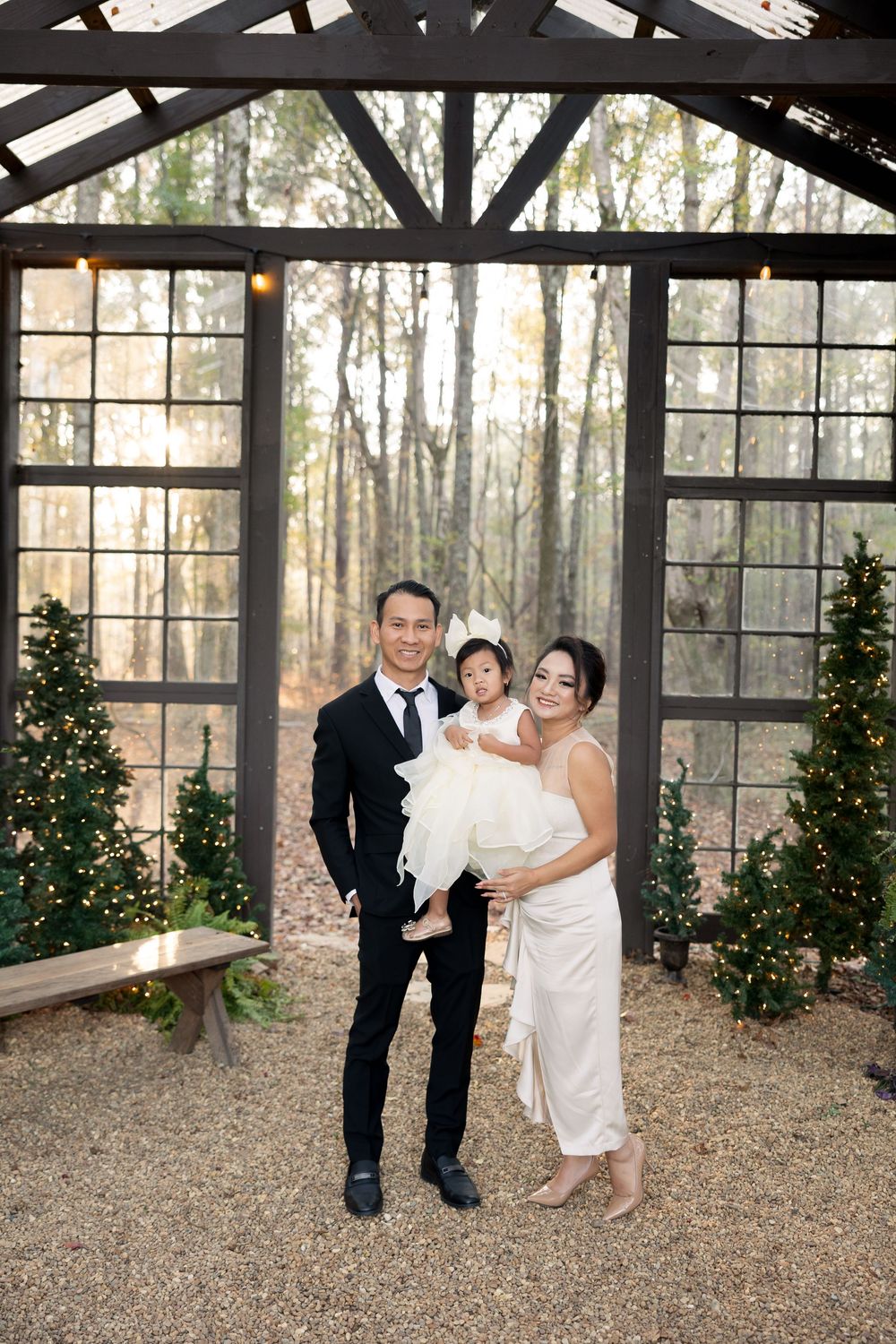 Wedding couple shares a tender moment in a rustic glass-walled pavilion surrounded by pine trees at sunset.