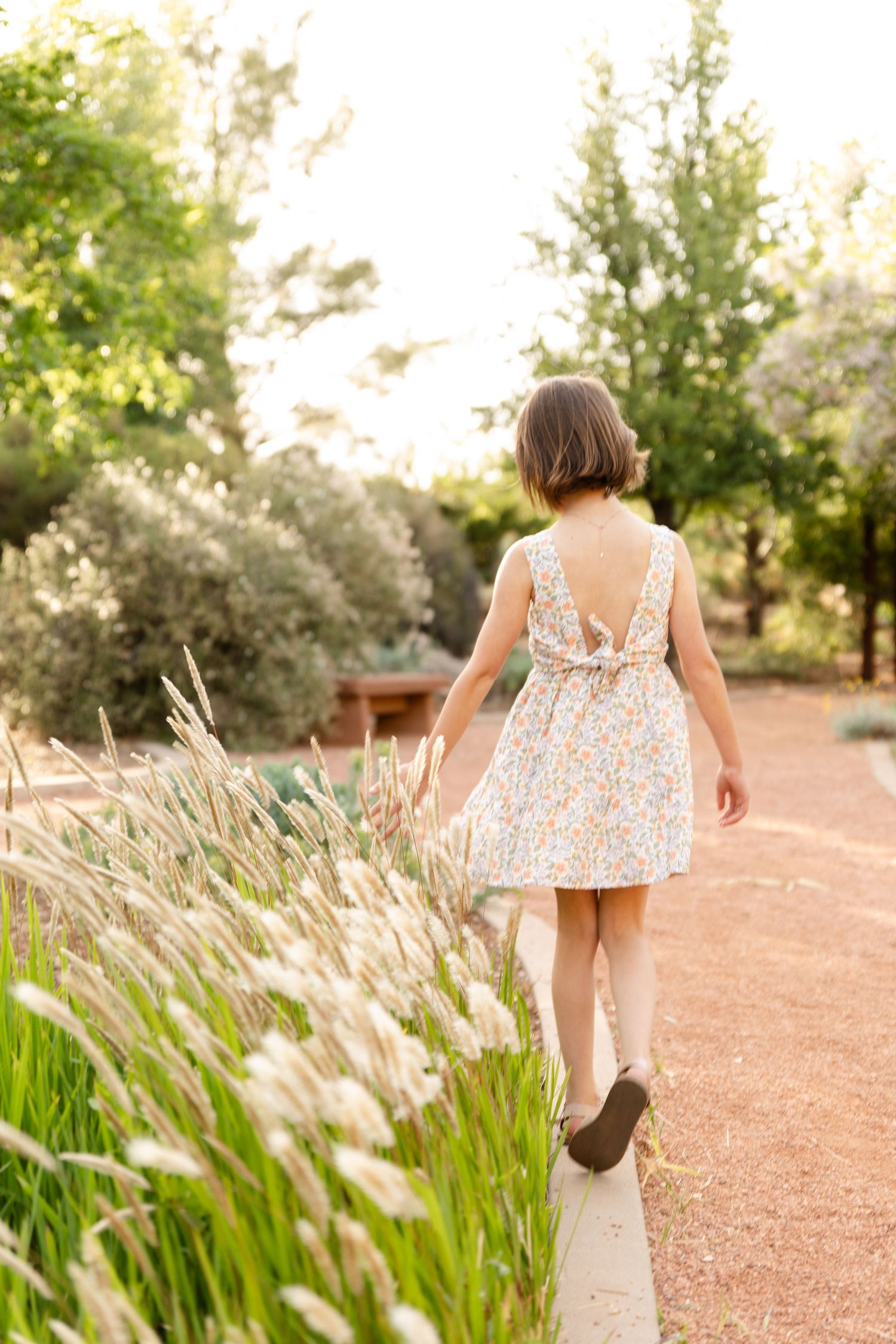 8 year old girl walking away from the camera hand brushing cattails waving in the wind