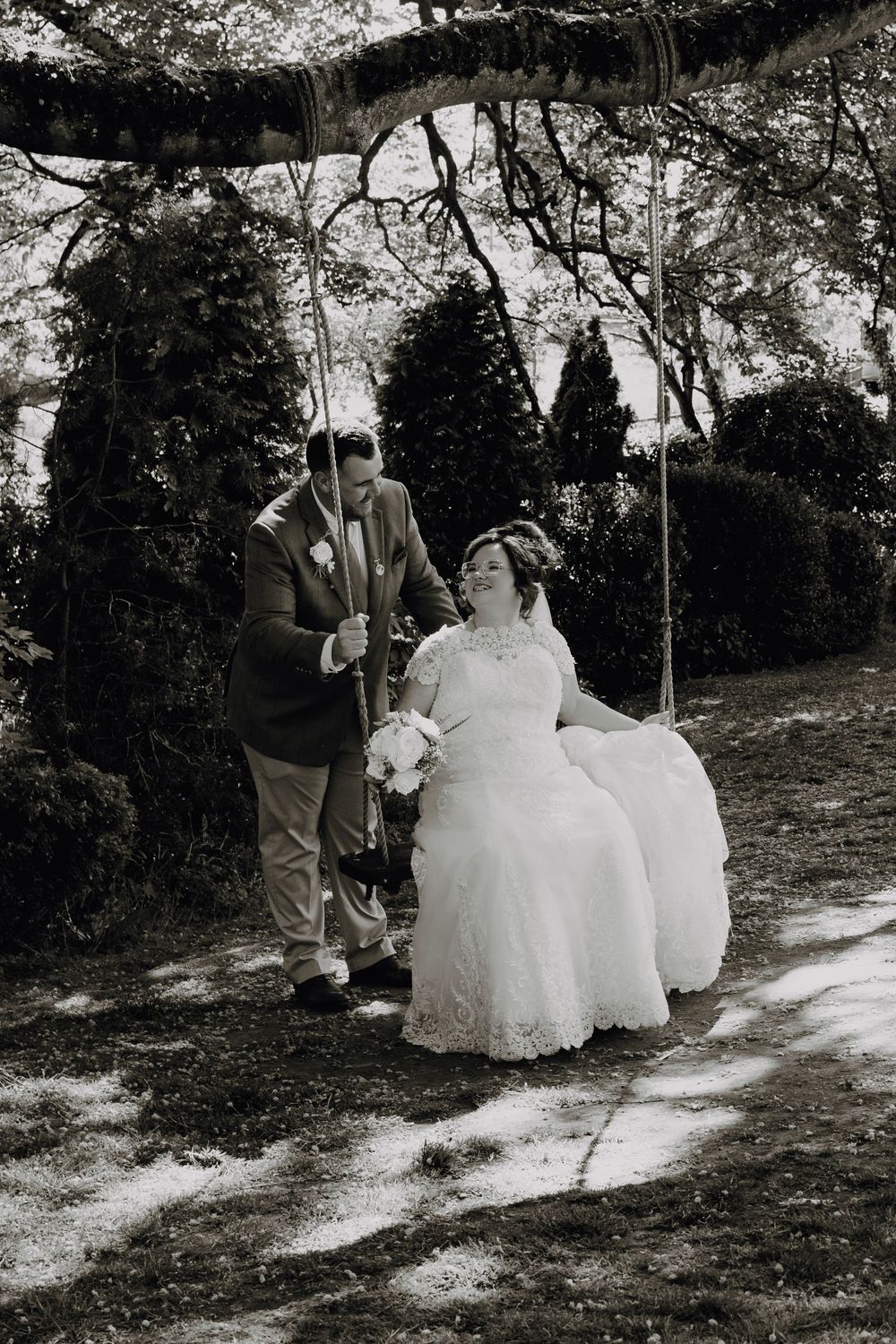 A black and white wedding photograph showing a couple sharing a sweet moment under blooming trees.