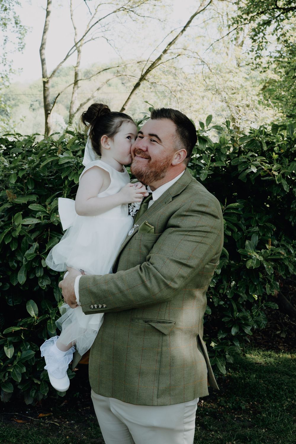A tender wedding day moment captured outdoors with greenery in the background.