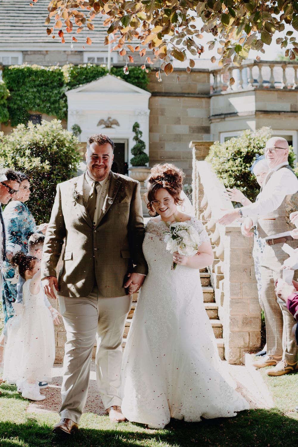 A joyous outdoor garden wedding ceremony with participants walking down stone steps surrounded by greenery and flowers.