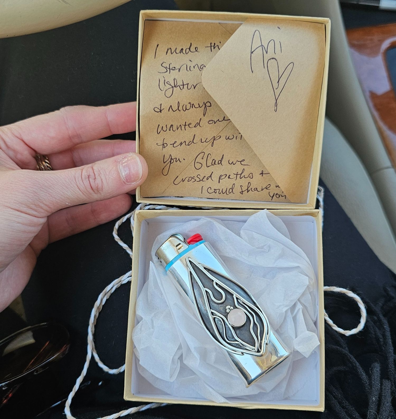 A cork-sealed glass bottle with decorative design sits in a small box with a handwritten note on its lid.