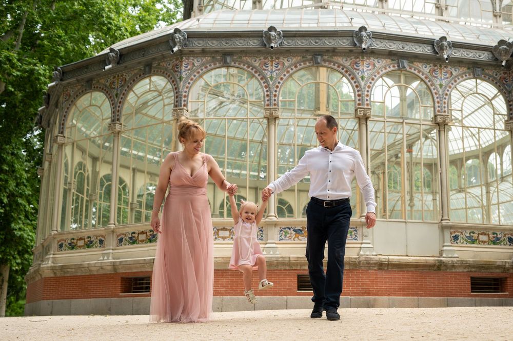 A family holds hands in front of a beautiful vintage glass conservatory structure in a garden setting.