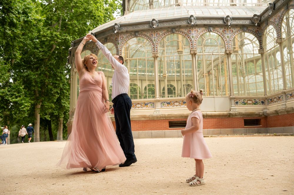 A graceful dancing scene in front of an ornate glass conservatory building with people in pink flowing dresses.