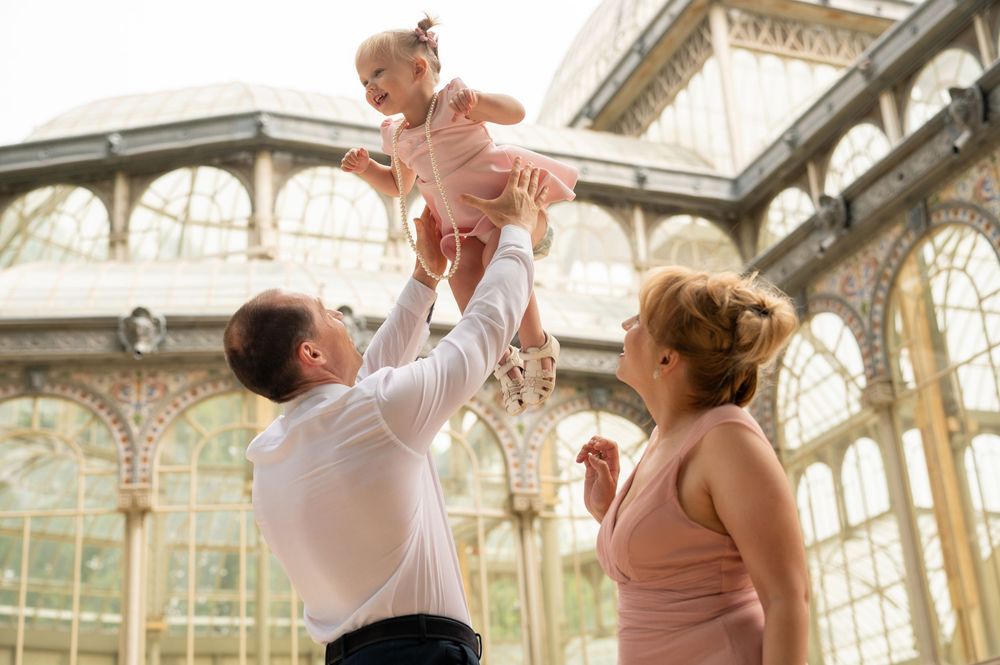 A happy moment shared between adults and a toddler being lifted up inside an elegant glass conservatory.