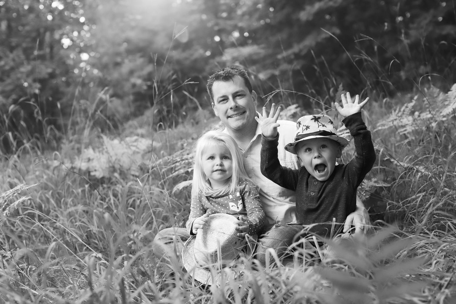 Black and white photo sitting together in tall grass outdoors, with two children and a playful mood. Lake Nebagamon Family Photographer