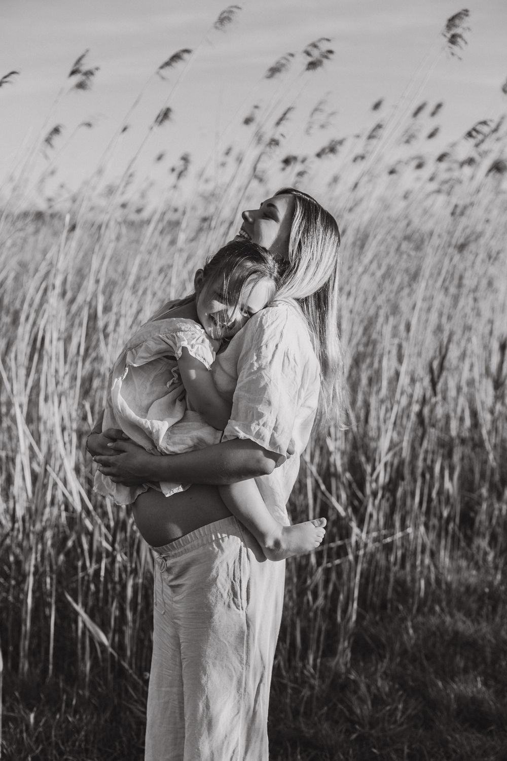 A tender embrace between parent and child silhouetted against a field of tall grass in black and white photography.