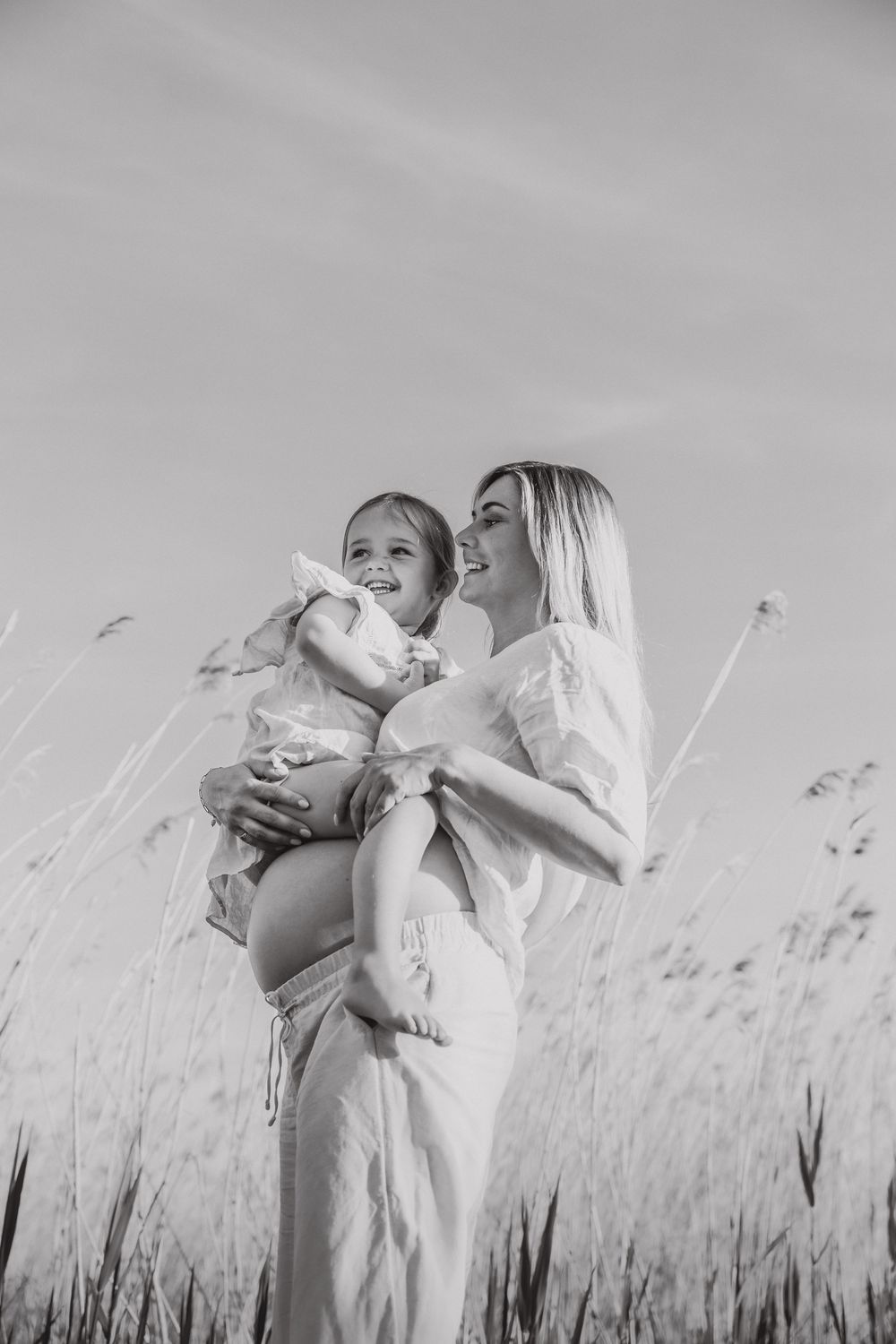Black and white photo of mother and child outdoors in a tall grass field on a sunny day.