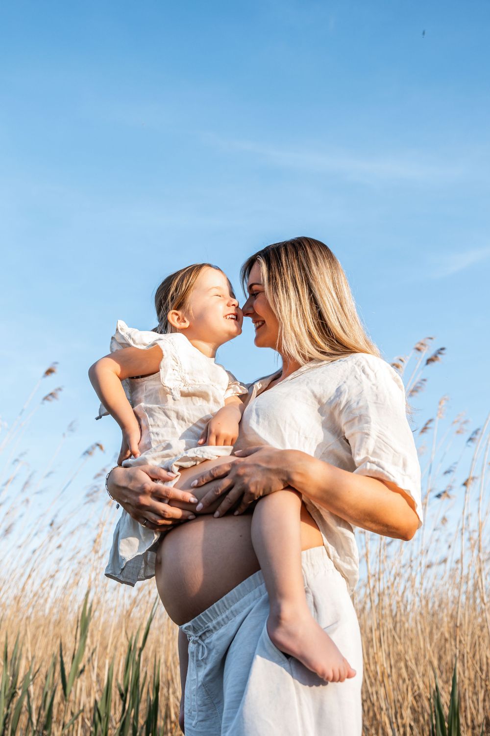 A tender moment shared between parent and child in a golden grass field against a bright blue sky.