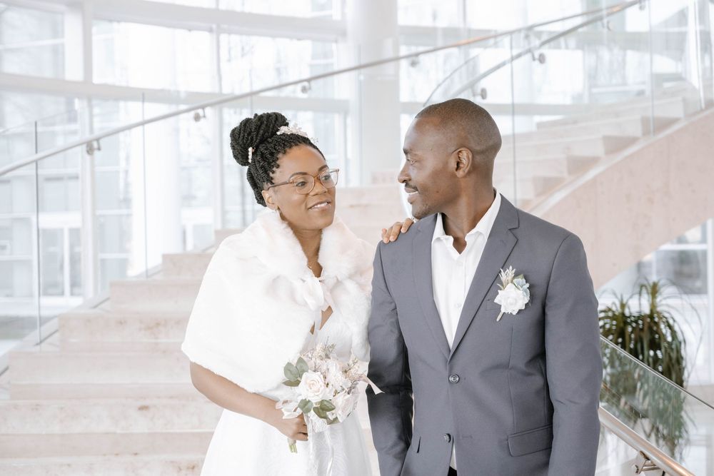 A couple shares an intimate moment in their wedding attire near a bright staircase.