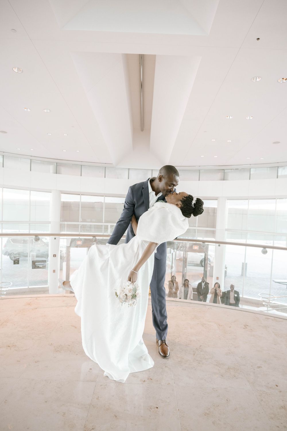 A romantic dip pose during a wedding dance in a bright modern venue with floor-to-ceiling windows.