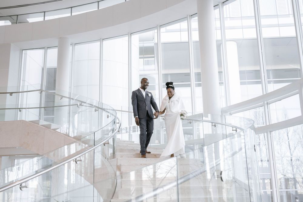 Elegant wedding couple poses on a bright white curved staircase in a modern building interior.
