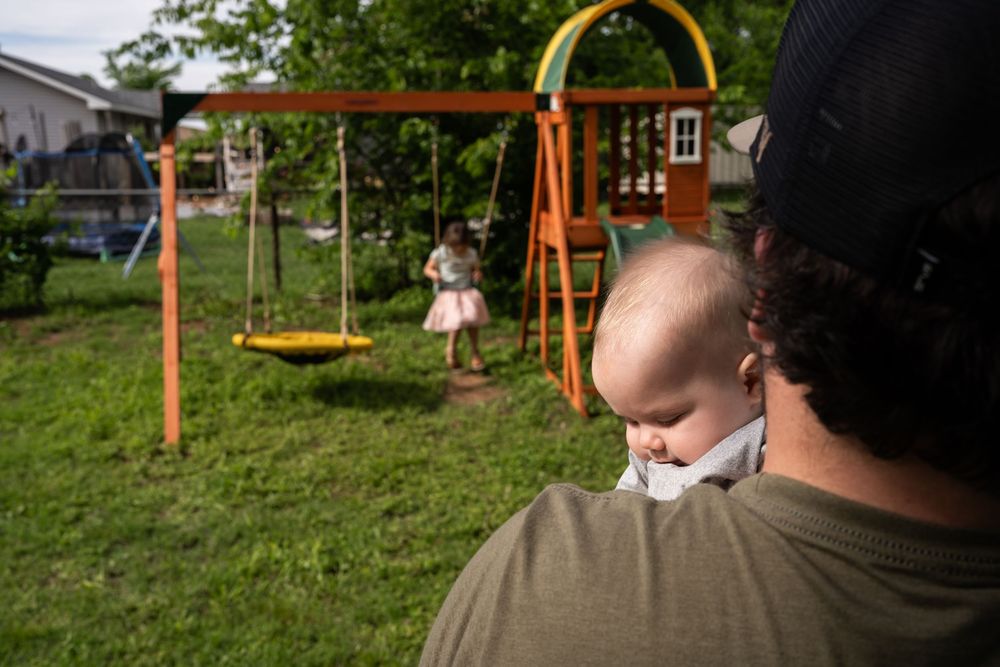 Looking of dads should at baby and sibling playing on swingset in backyard family photography session.