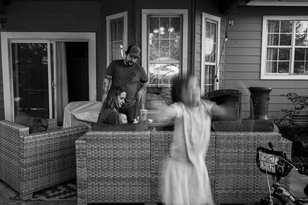 Kid jumping on trampoline while mom feed baby and relaxs on outdoor couch. Family Photography