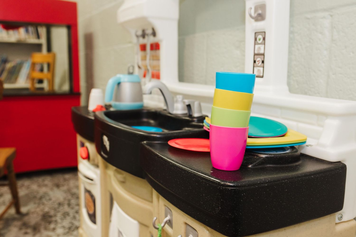 Colorful plastic cups and plates sit on a black counter surface in a preschool play kitchen setting.