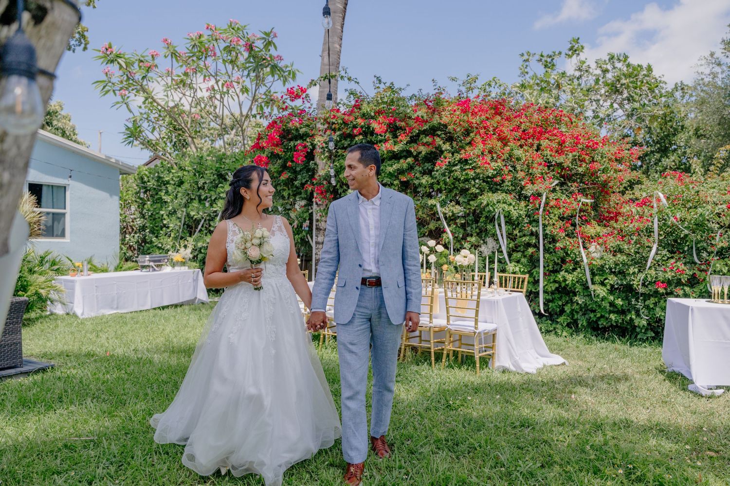 A romantic outdoor garden wedding ceremony setup with vibrant red bougainvillea flowers blooming on an archway.