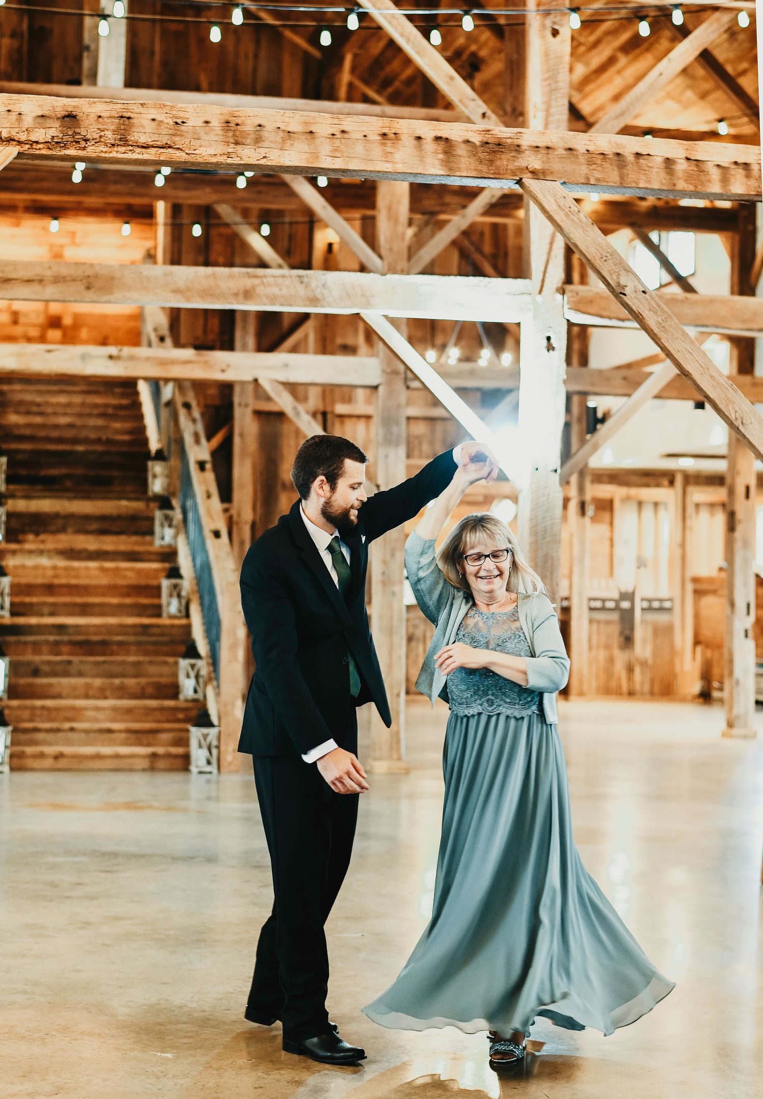 the groom spins his mother for his dance with her at his wedding reception in the rustic barn