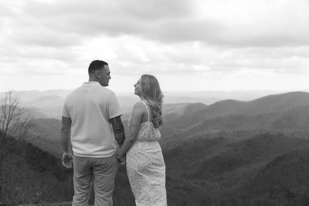 A couple stands together overlooking the blue ridge mountains landscape with rolling hills in black and white.