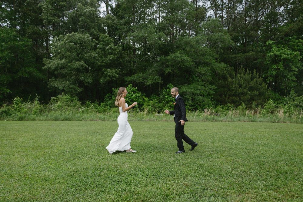 A couple dances and plays casually in a grassy field surrounded by lush green trees on their colorado springs elopement day