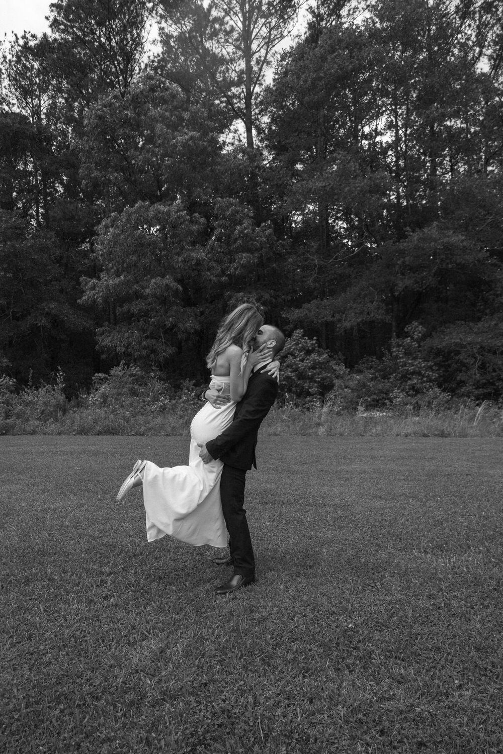 A romantic black and white photo of a couple embracing in a field with trees in the background on their telluride elopement day