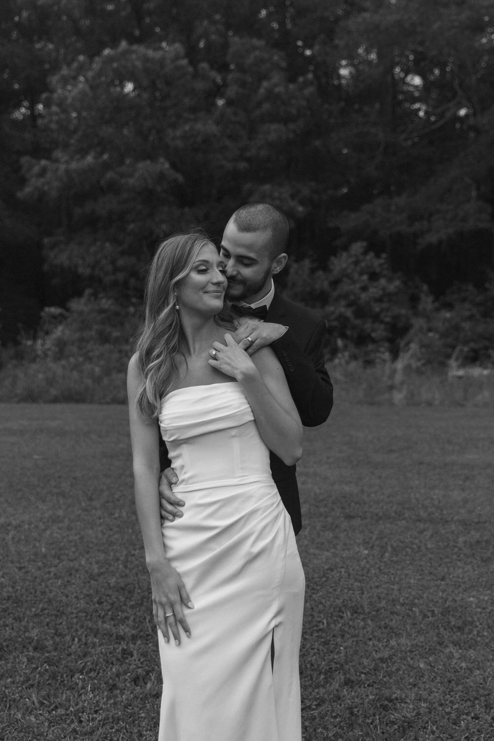 A romantic black and white elopement photo shows a couple embracing on a grassy field with trees in background in colorado springs