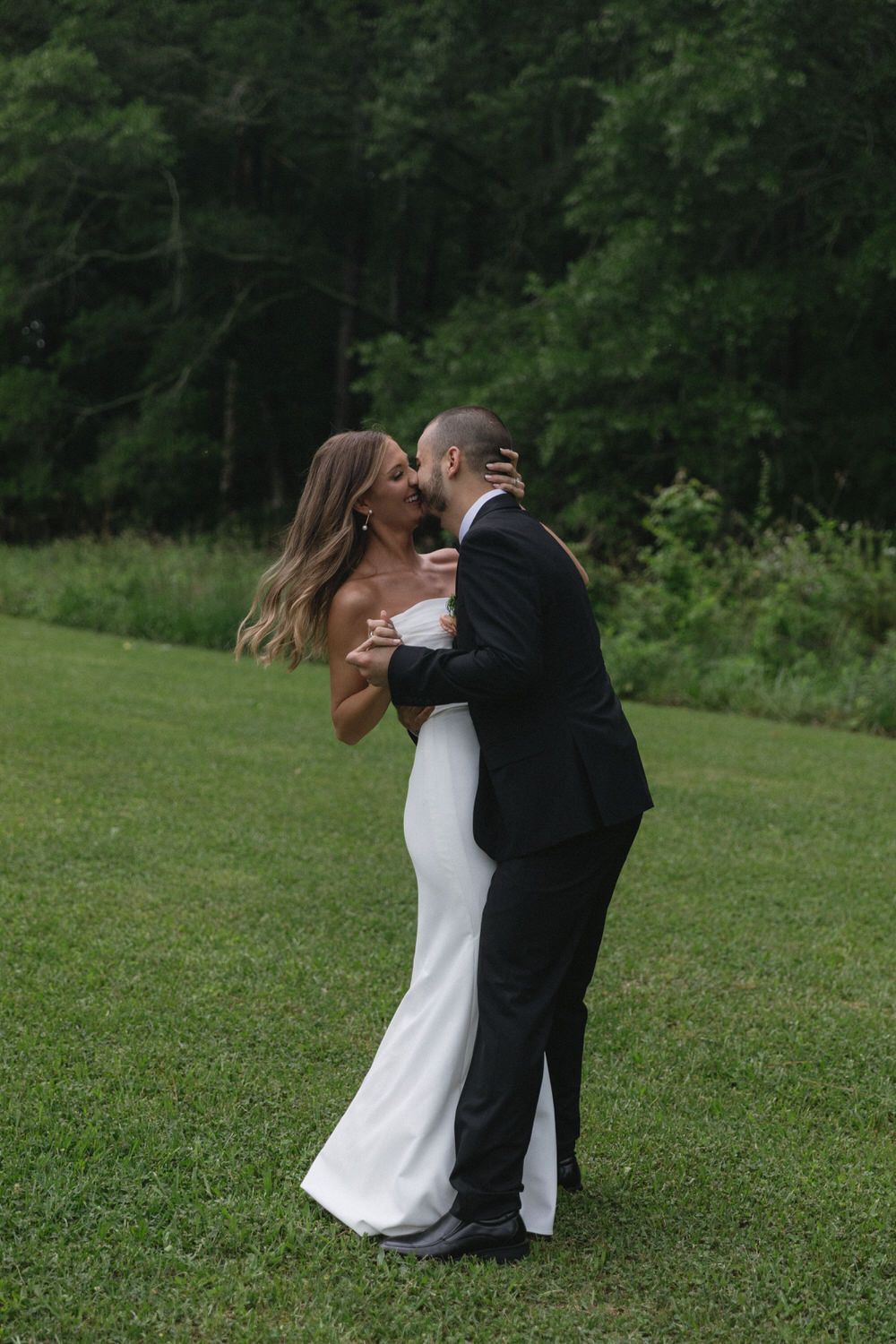 A couple in wedding attire embrace lovingly in a scenic outdoor setting with lush green trees in the background in colorado springs