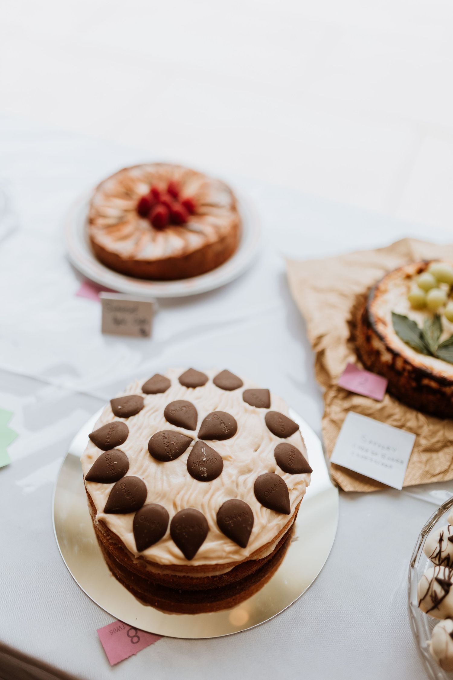 Chocolate layer cake decorated with heart-shaped candies on white cake stand with other desserts in background.