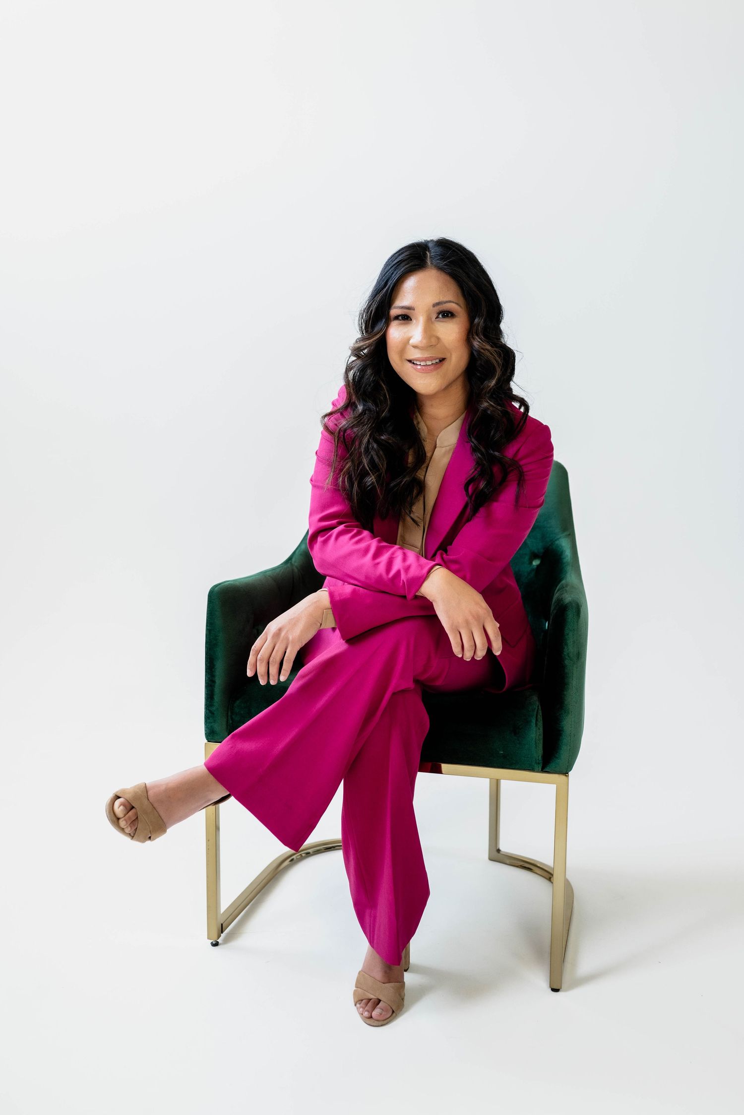 Person seated in emerald velvet chair wearing vibrant magenta power suit.