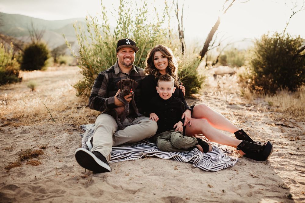 People and dogs relaxing on blanket in desert setting during golden hour.