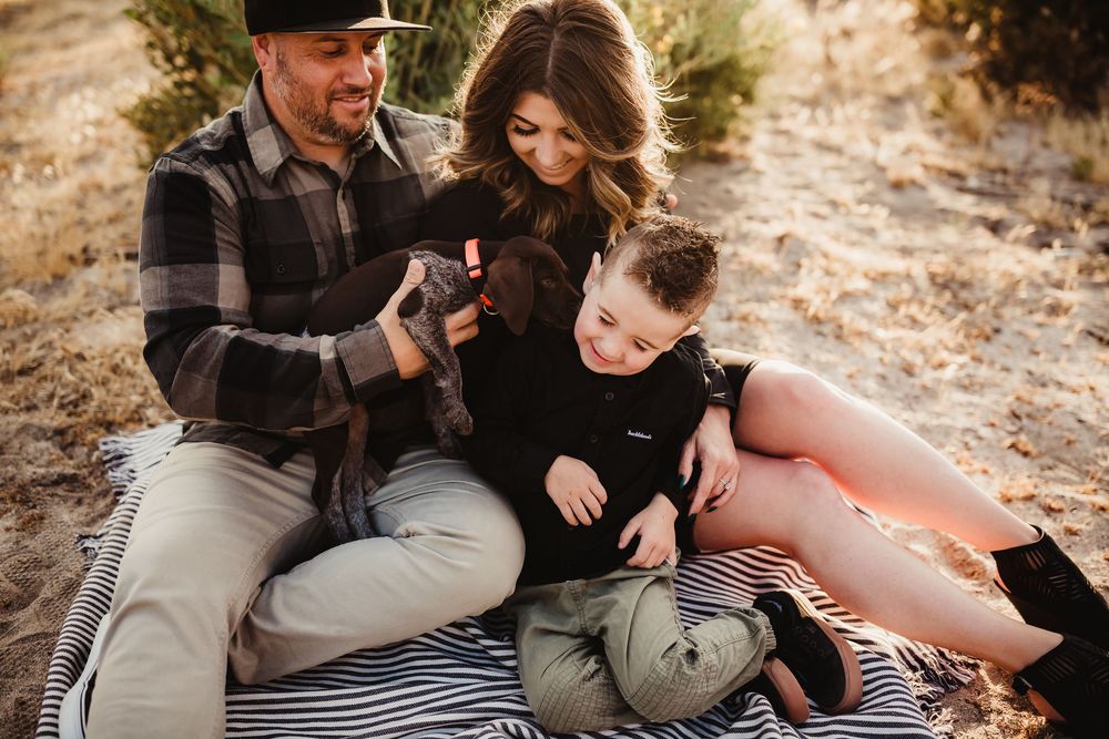 A couple relaxes on a blanket with their dachshund during a desert photoshoot.