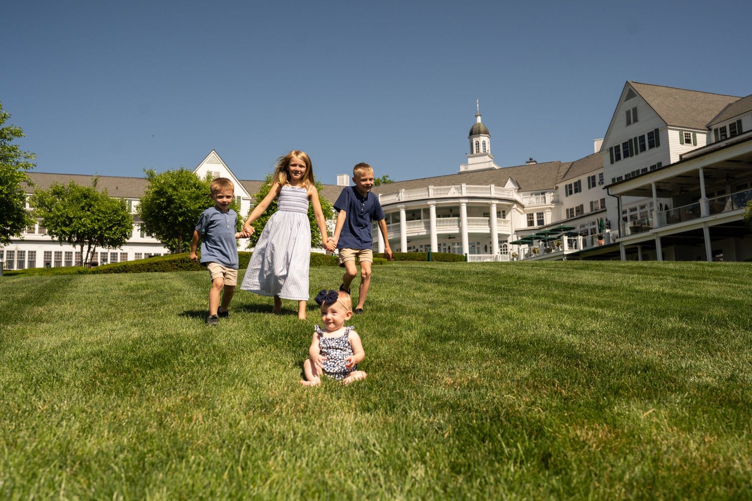 People playing and running on a grassy hillside during a summer day with white buildings visible in the background.