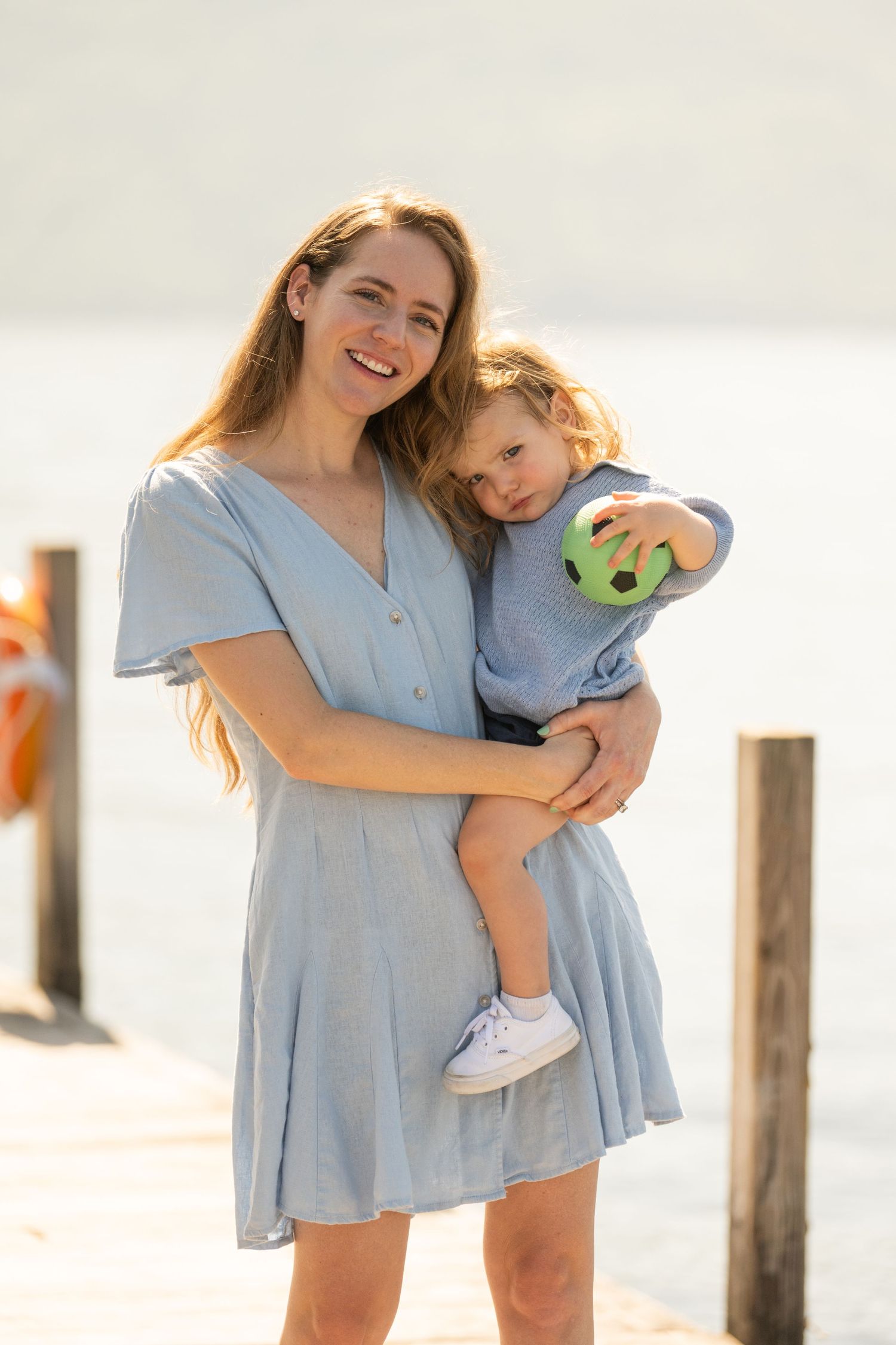 Parent and child in matching blue dresses share tender moments at the beach during a sunset photoshoot.