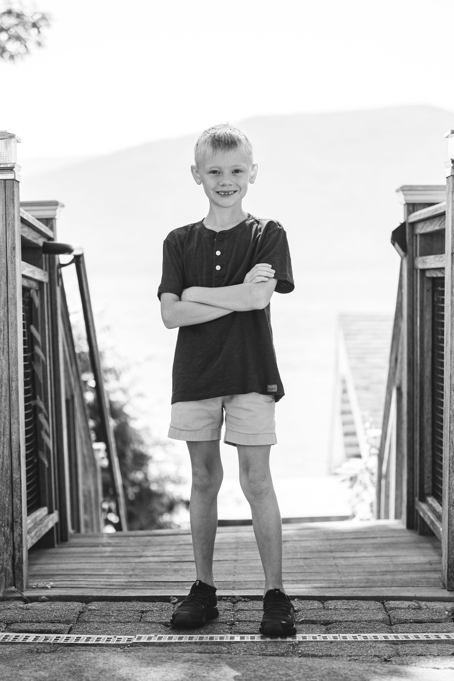 Black and white portrait of young child standing confidently on wooden deck wearing casual summer attire.