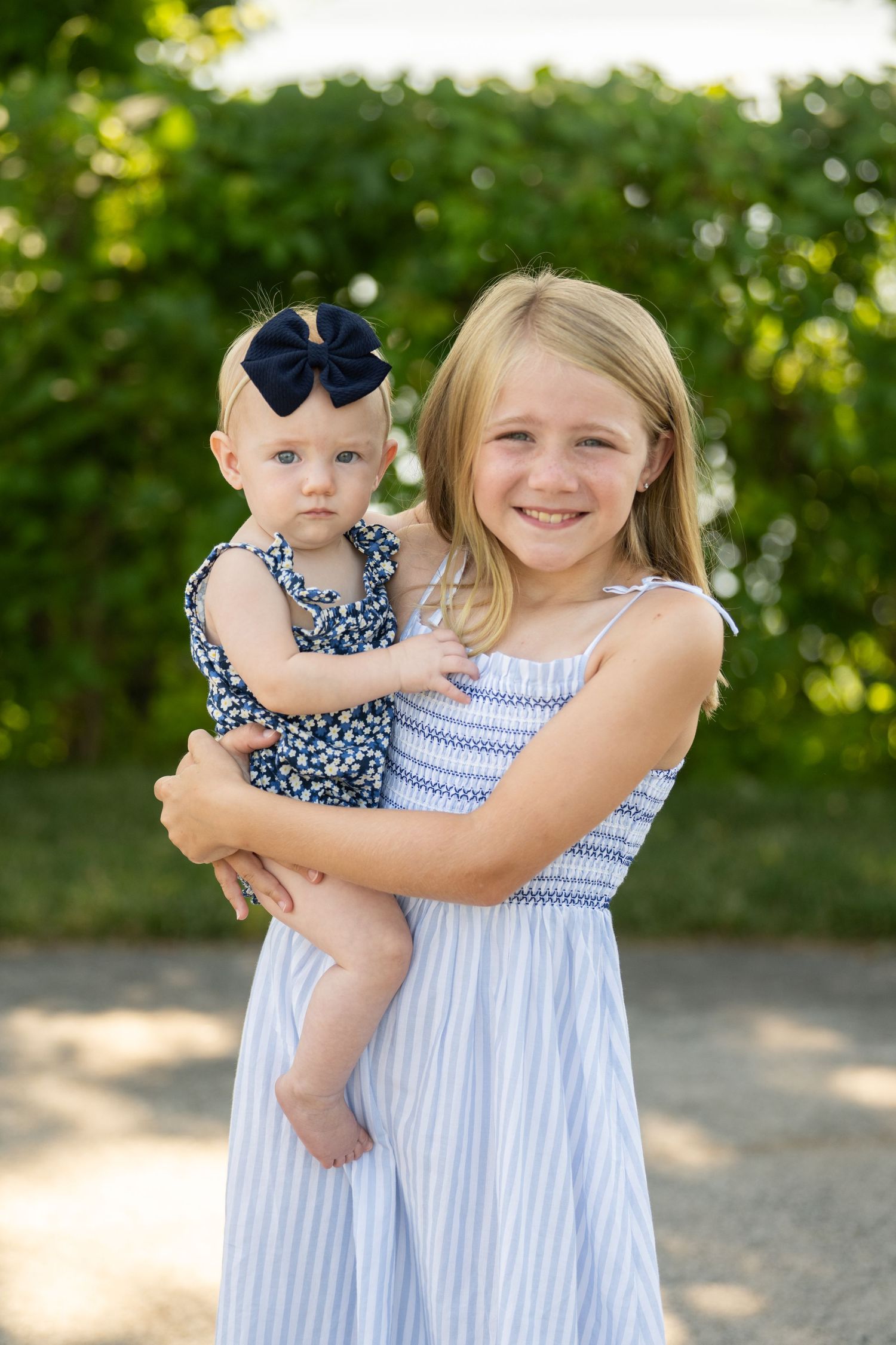 A sweet outdoor portrait of siblings in coordinating blue and white summer dresses on a sunny day.