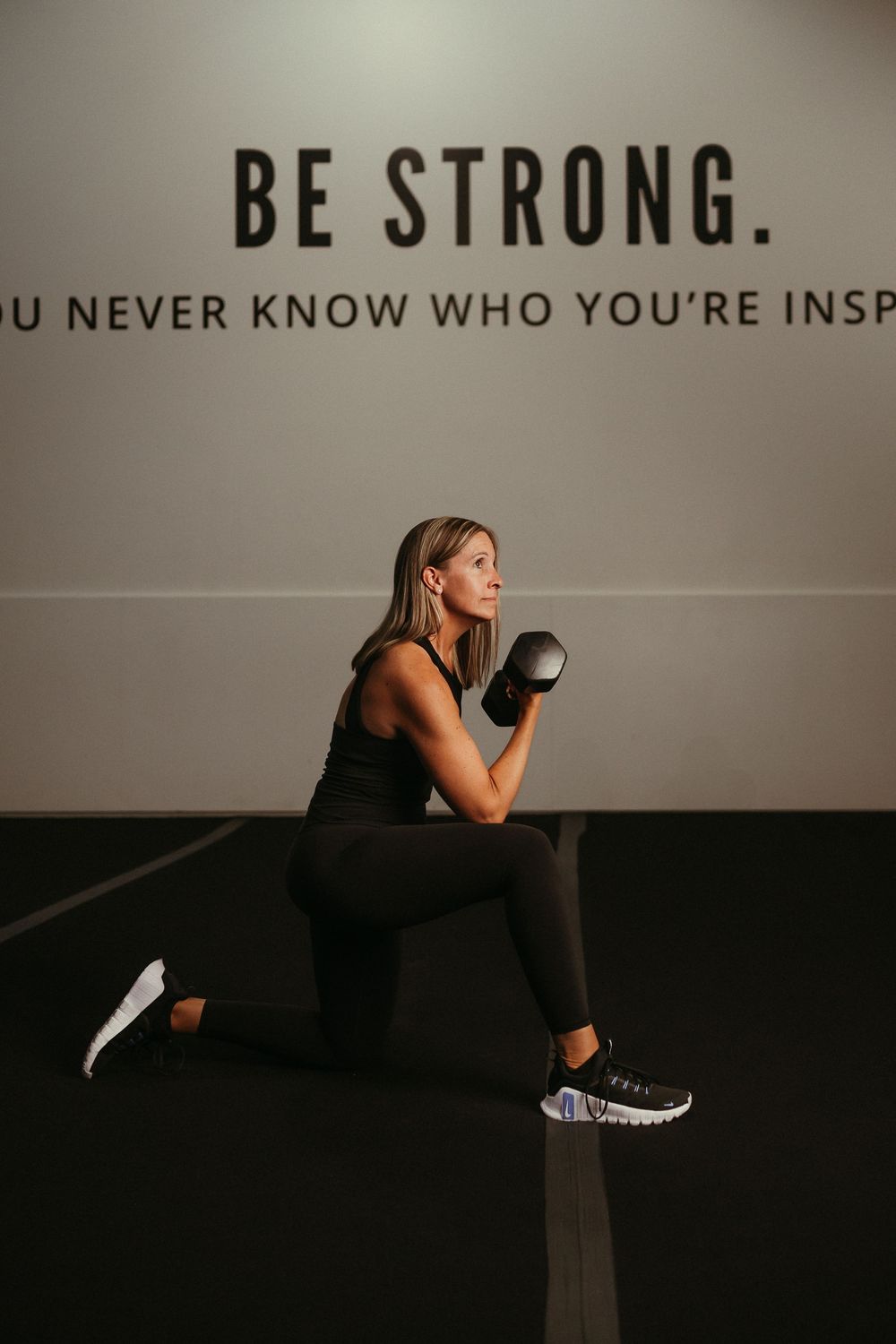 Motivational gym wall with 'BE STRONG' text and a sequence of workout poses shown in black and white.