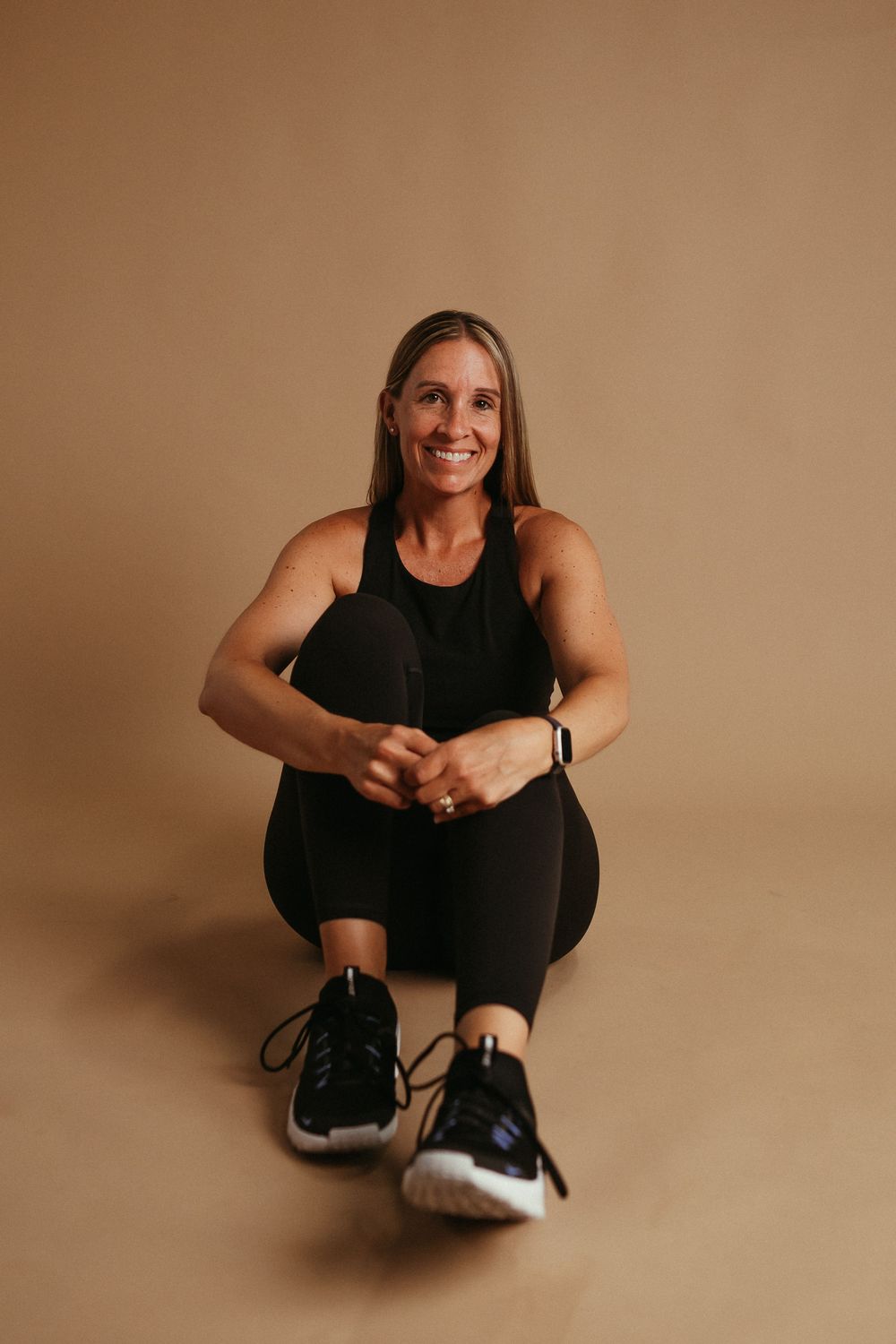 Athletic figure in black workout attire sits on brown backdrop in series of dynamic stretching poses.