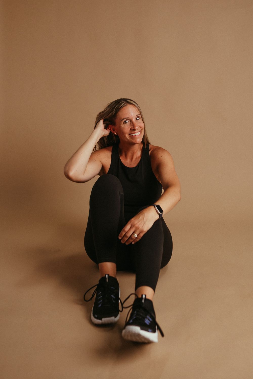 Person in black athletic wear sits on brown seamless backdrop through series of casual lifestyle poses and movements.