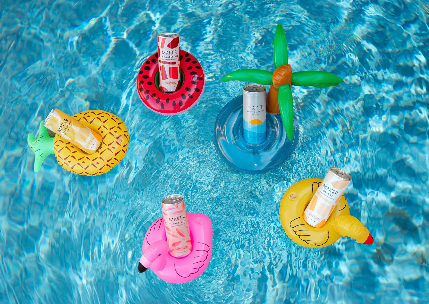 Colorful inflatable drink holders including pineapple, flamingo and palm tree designs floating in bright blue pool water.
