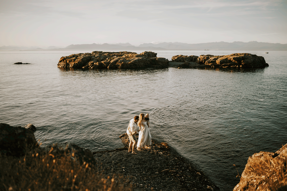 Candid gif of parents holding baby and throwing rocks in ocean Neck Point Park Nanaimo family photography by Comox Valley photographer