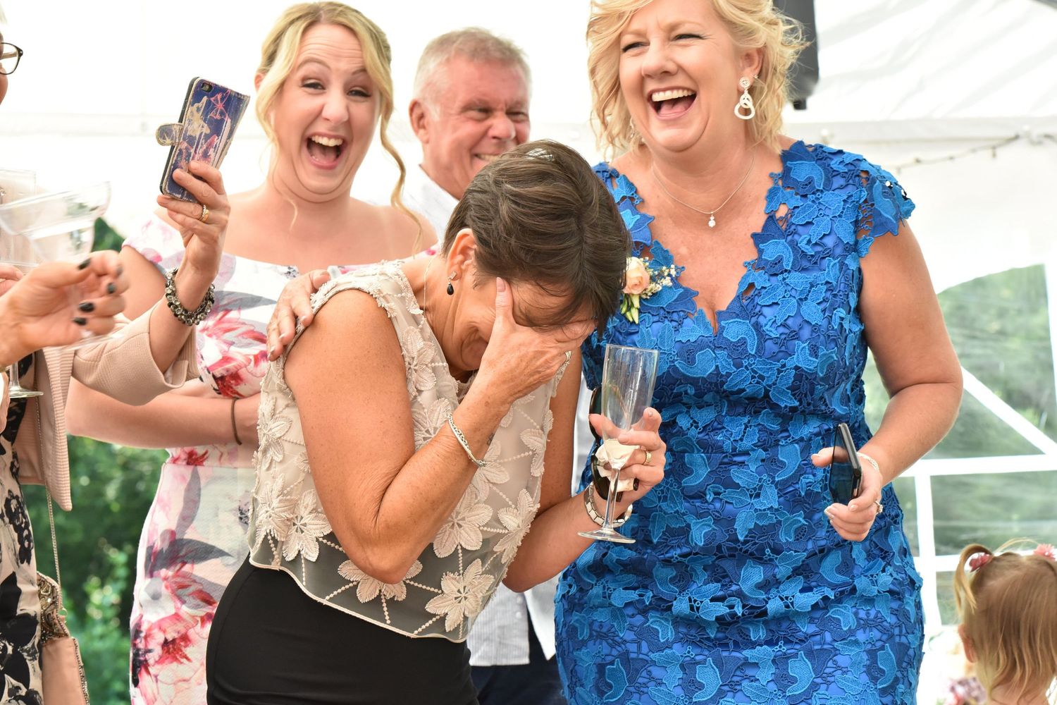 Mother of bride holds head in hand during speeches, everyone around her is laughing
