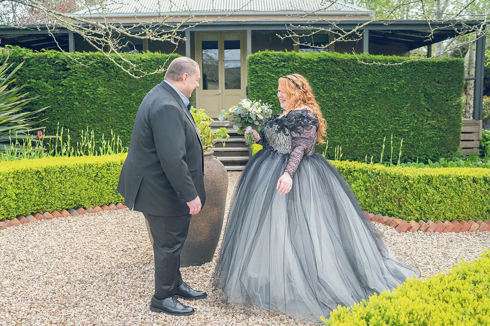 A couple stands together in a formal garden with trimmed hedges, the gown in silvery gray tulle creating an elegant silhouette.