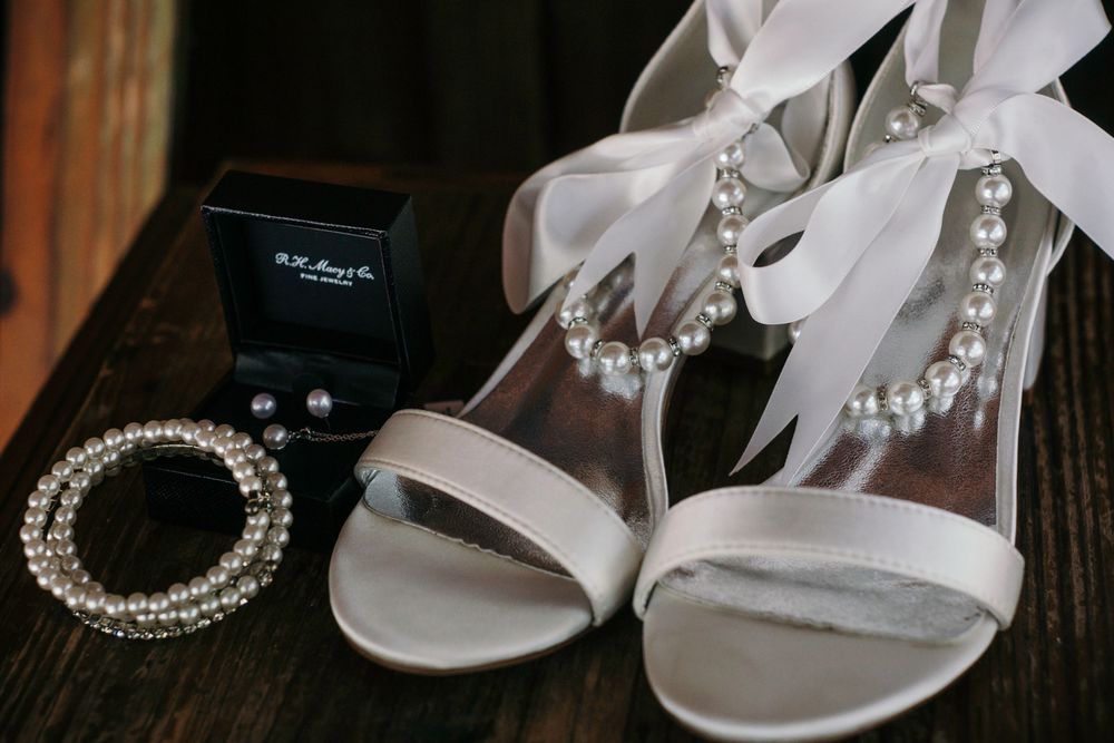 Elegant white bridal shoes and jewelry displayed on dark wooden surface.