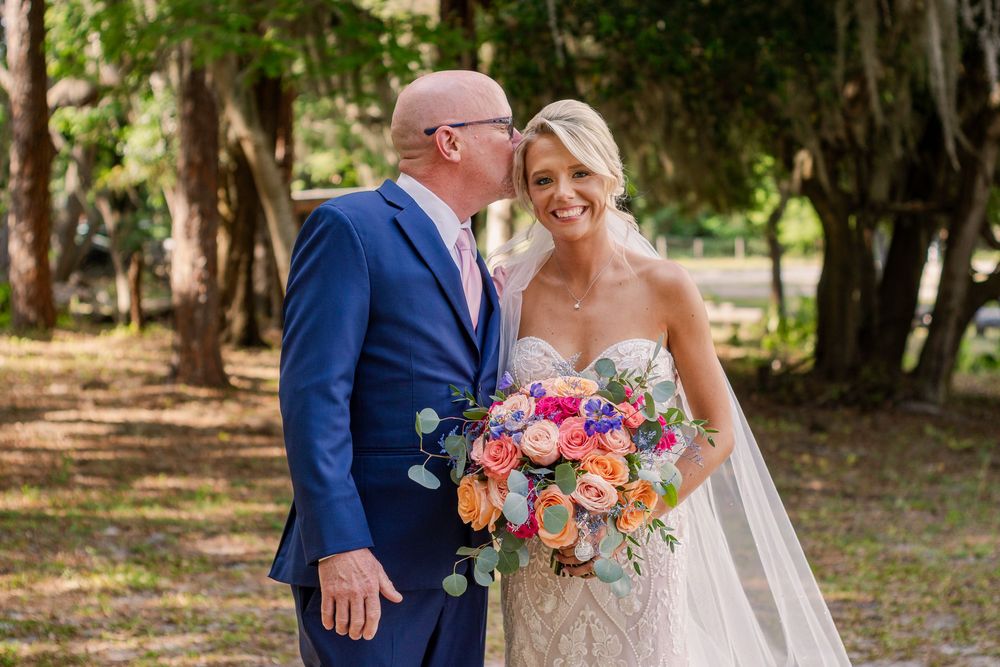 Wedding couple shares joyful moment outdoors under natural tree canopy.