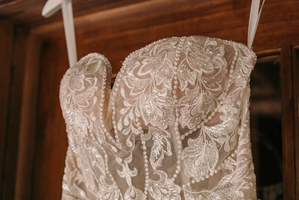Close-up detail of an elegant white lace wedding dress bodice on a wooden hanger.