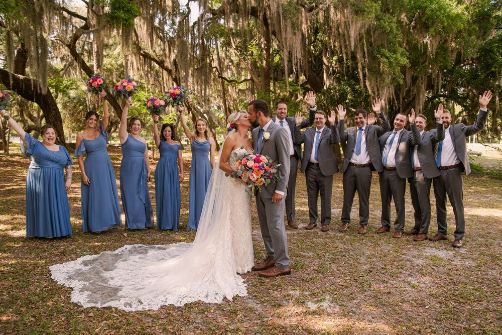 Wedding party in navy and grey attire posed beneath Spanish moss trees for formal group photo.