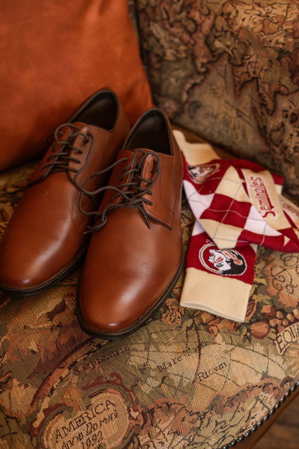 Brown leather dress shoes and red argyle socks arranged on vintage world map background.
