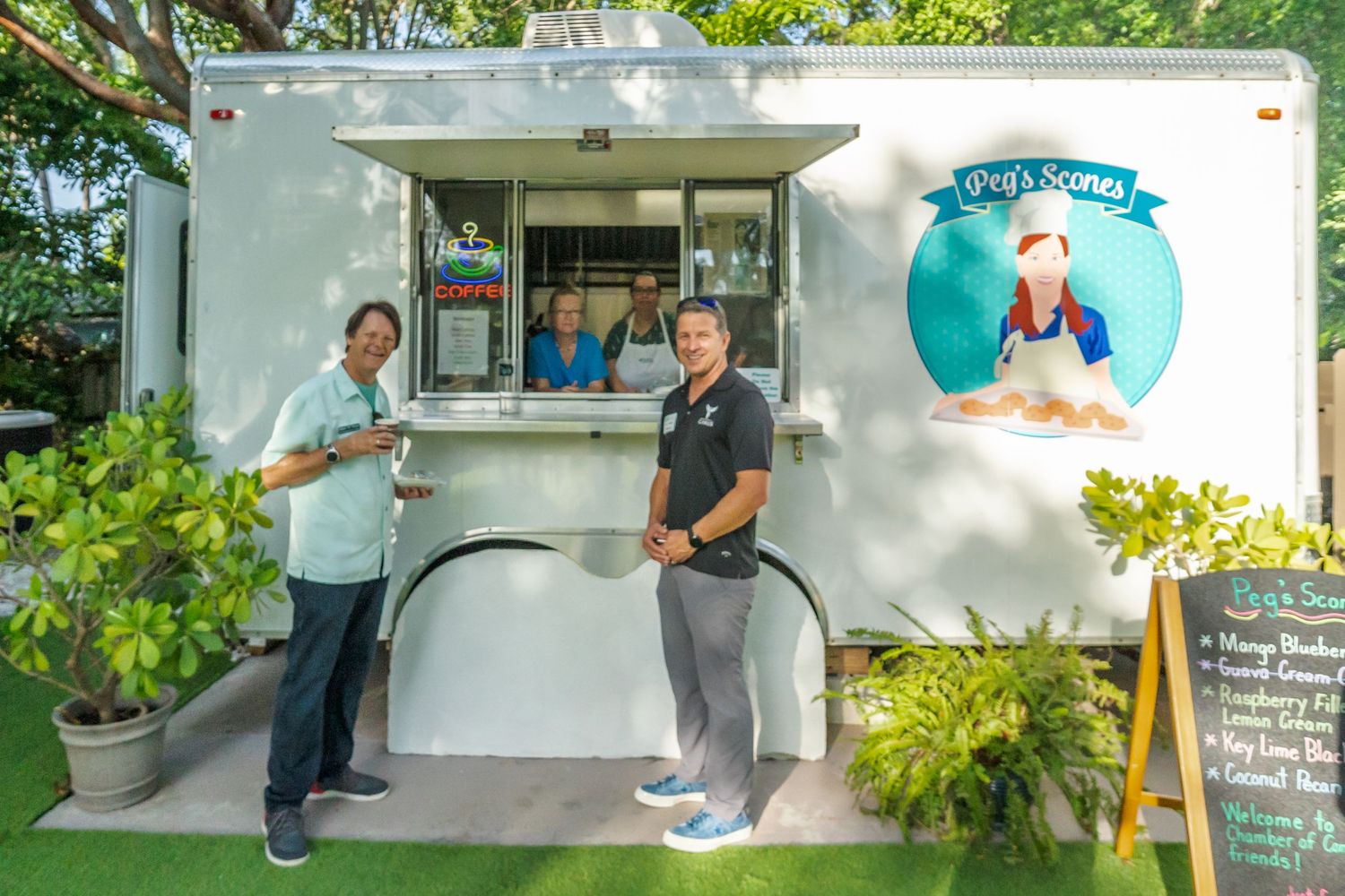 A white concession stand or kiosk building with people gathered outside under tropical landscaping.