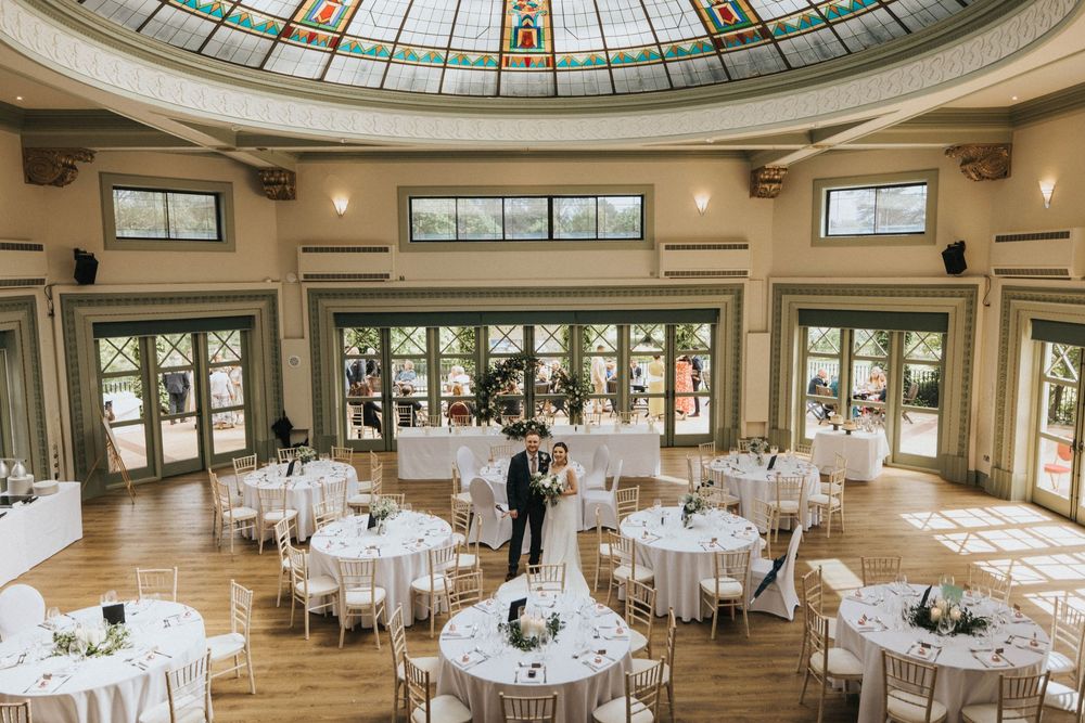 Elegant reception hall with domed glass ceiling and round tables set for a wedding celebration.