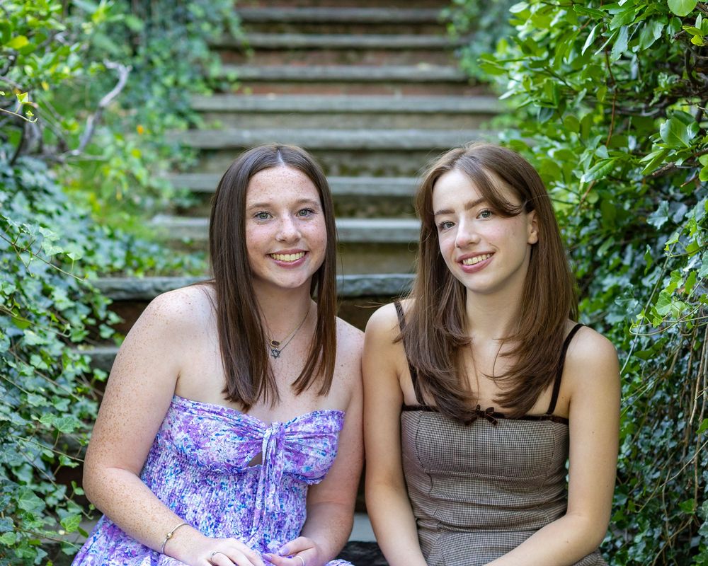Two people sitting together on stone stairs surrounded by lush green foliage in summer.