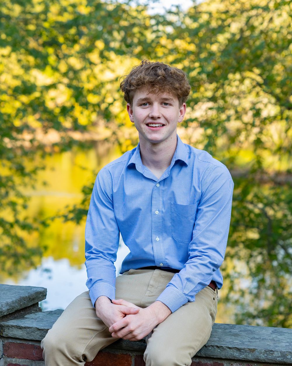 High school senior portrait session featuring someone in a blue button-down shirt and khakis sitting on stone steps outdoors.